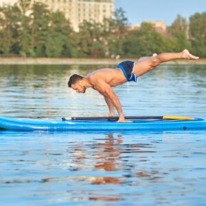Man practicing yoga, doing balance body weight smimming on paddle board.