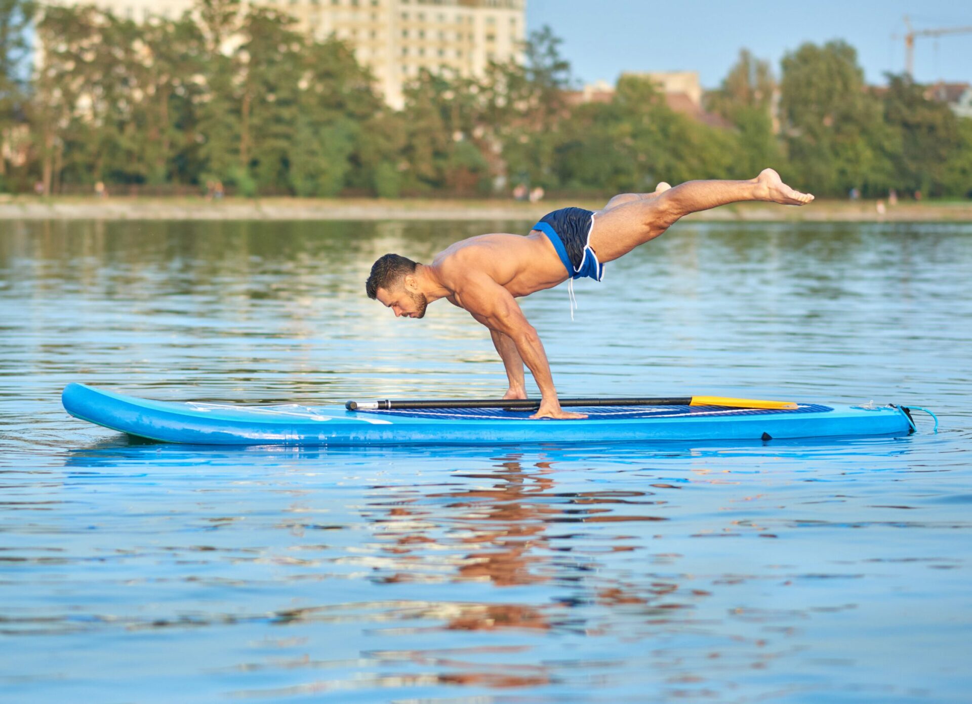 Man practicing yoga, doing balance body weight smimming on paddle board.